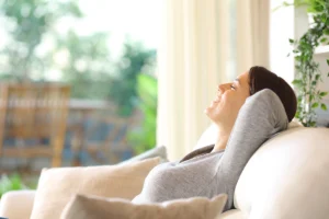Woman relaxing on a couch in a bright living room, representing cleaner indoor air and comfort for homeowners asking would an air purifier help with dust